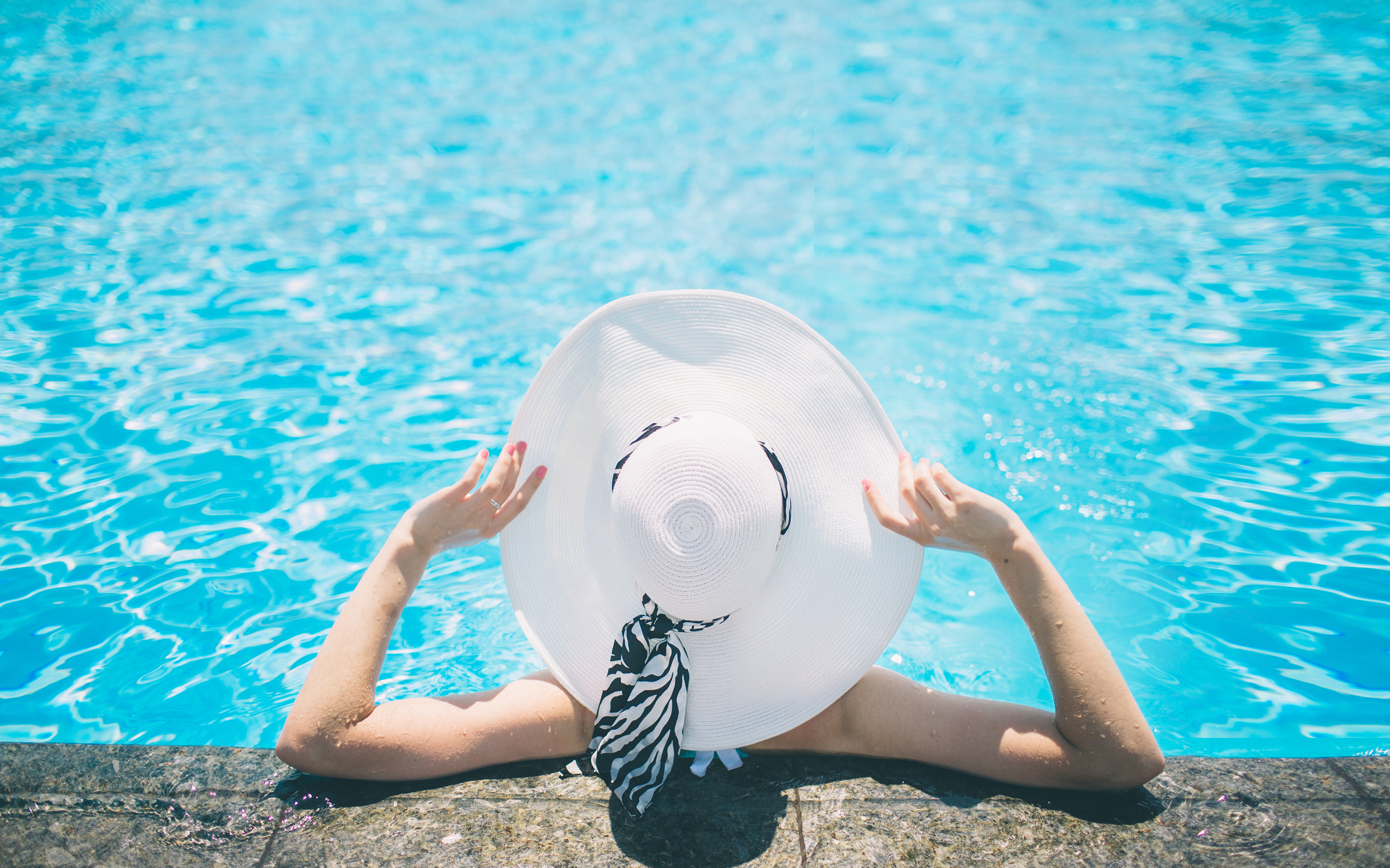 Woman lounging in the pool wearing a hat.